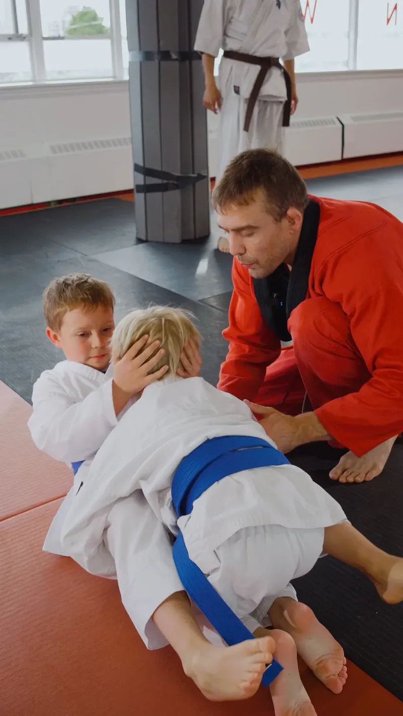 Coach coaching two young students through a jiu-jitsu position on the mats