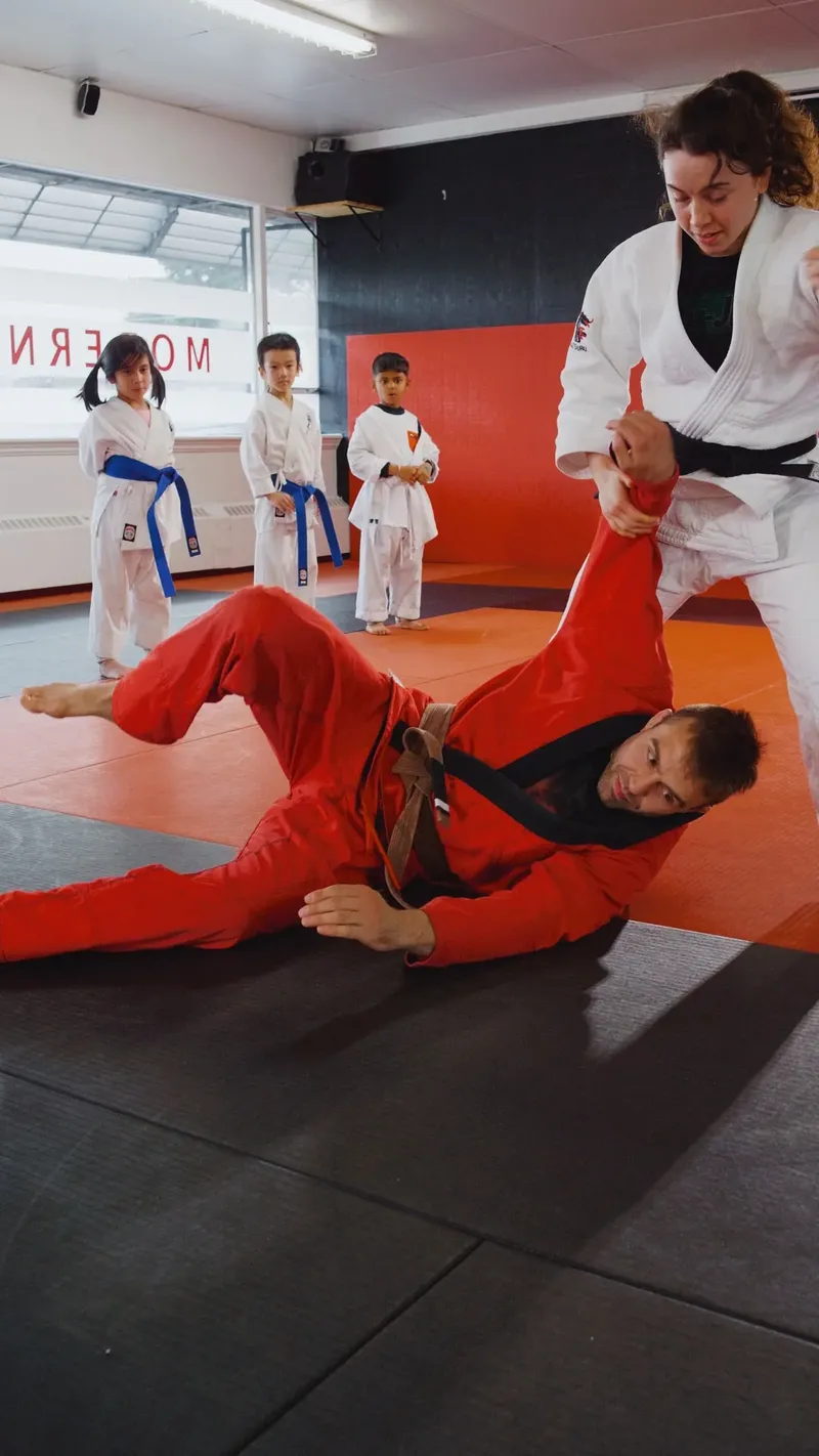 Kids watching a student complete a throw on a coach during grappling practice