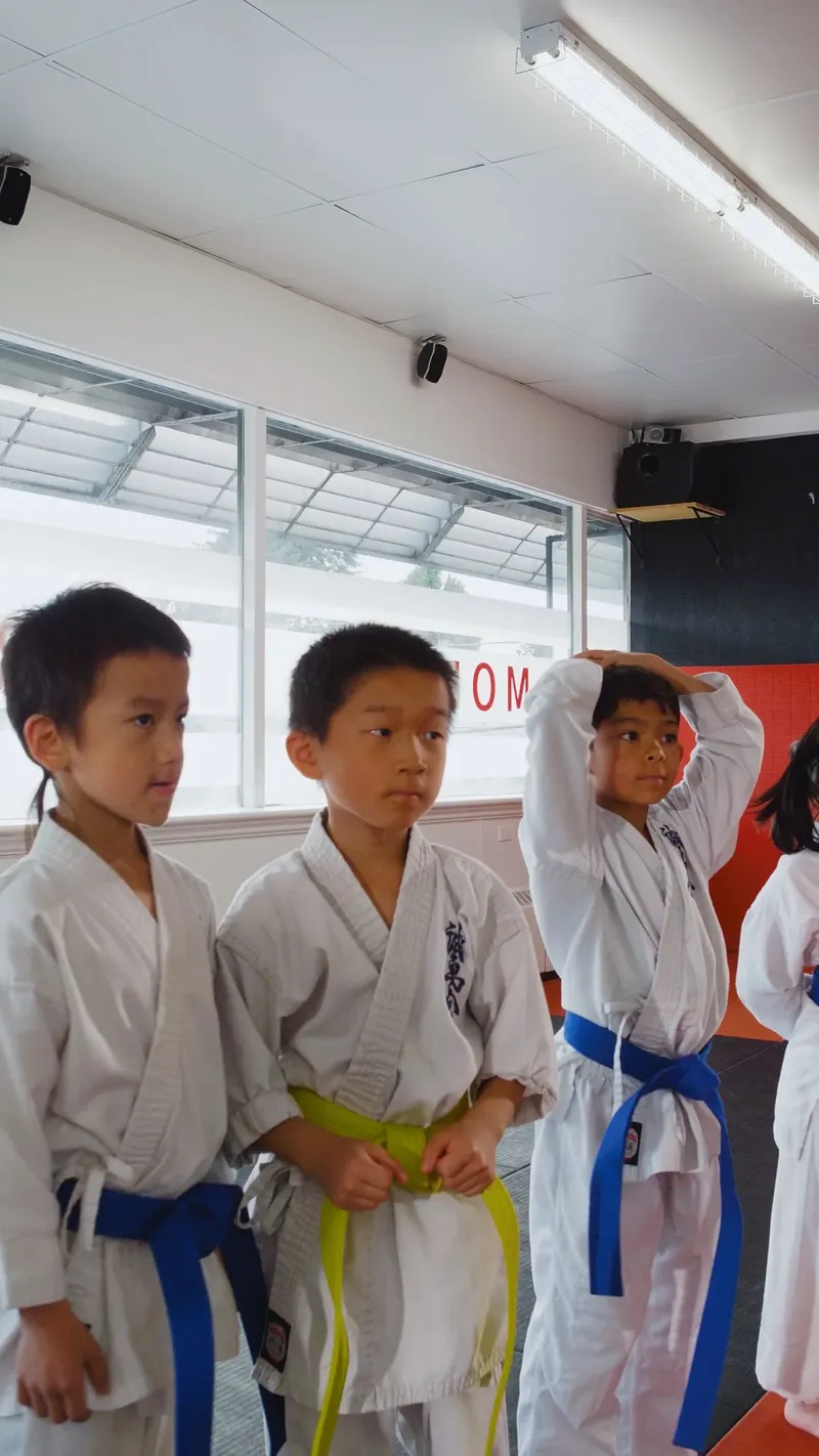 Three focused kids in karate uniforms listening to instruction at the New Westminster dojo
