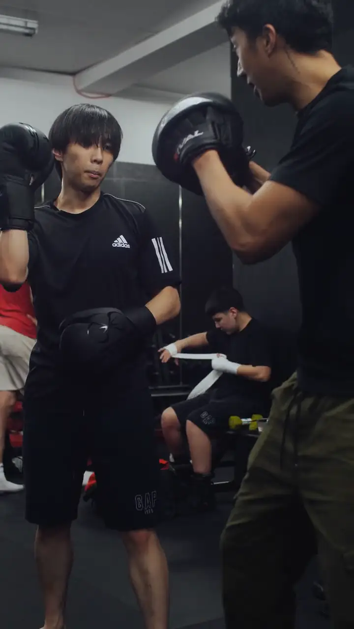 A student in gloves throwing a jab to focus mitts during a Modern Warrior boxing class.