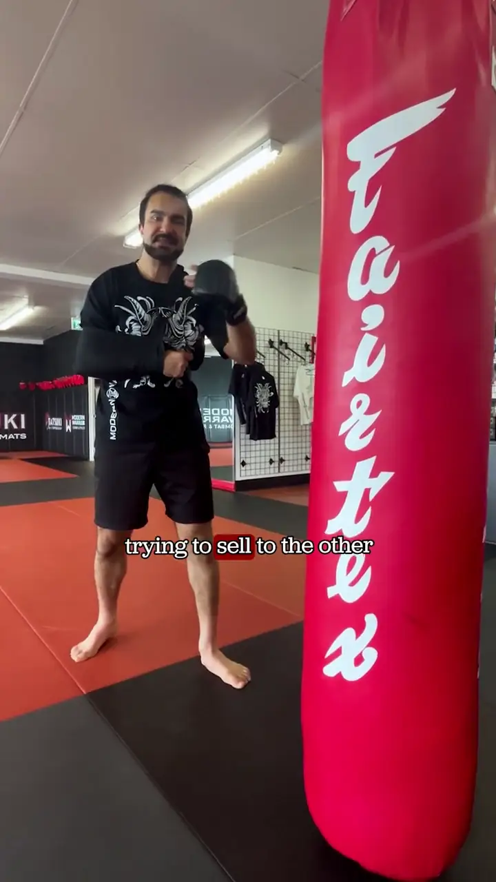 A Modern Warrior coach in a black shirt demonstrating a jab-feint mistake on the heavy bags.