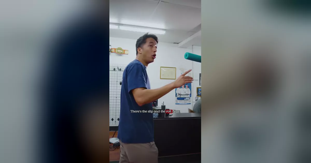 A Modern Warrior coach in a navy shirt demonstrating boxing head movement with a teal foam noodle on the gym floor.