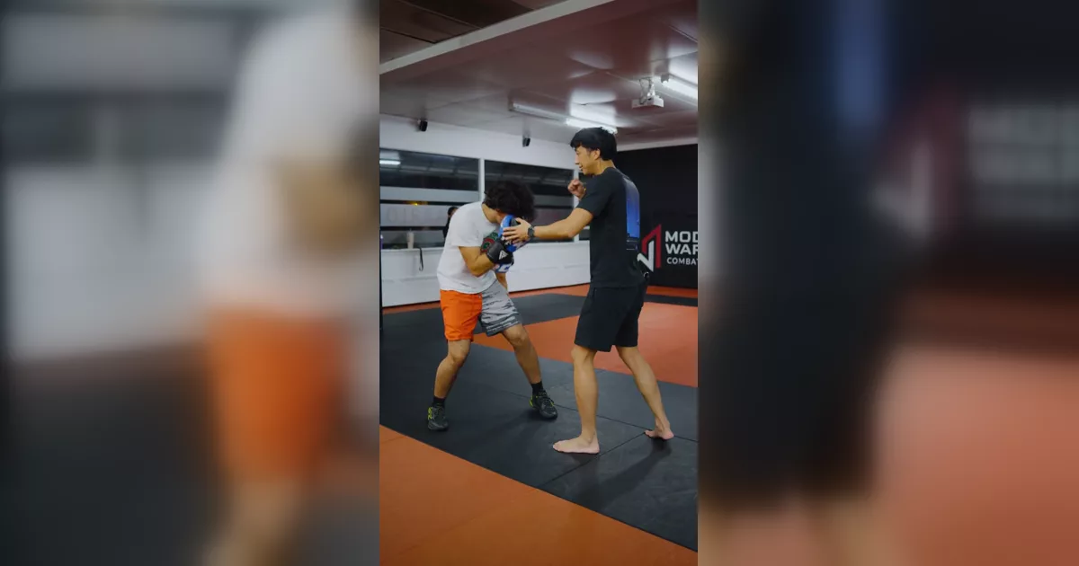 Coach demonstrating a boxing defence sequence with a gloved partner on the mats.